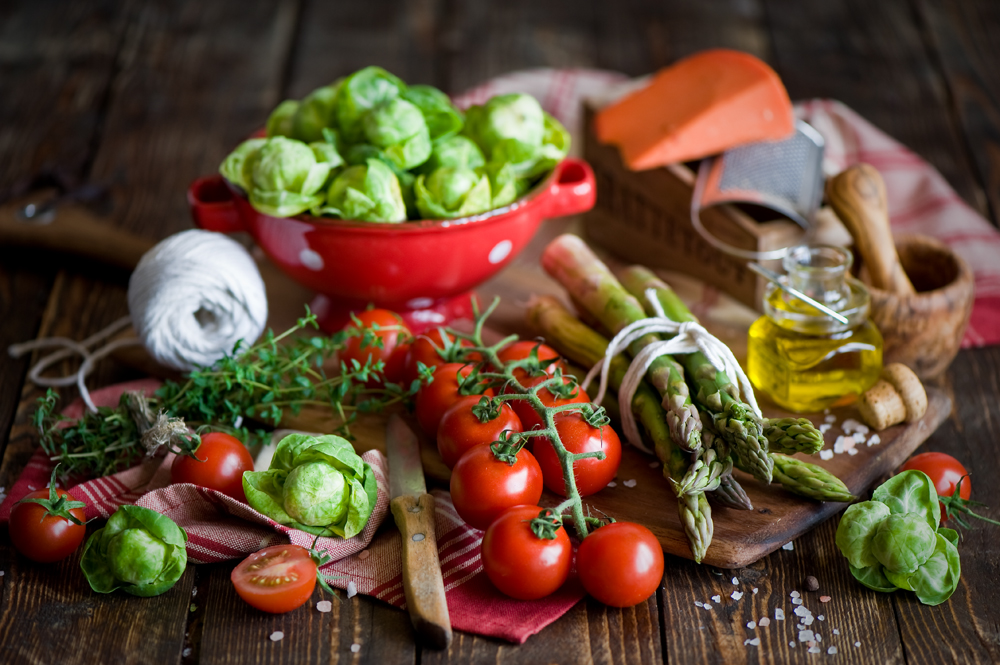 Wooden table covered in vegetables, olive oil, and cooking utensils