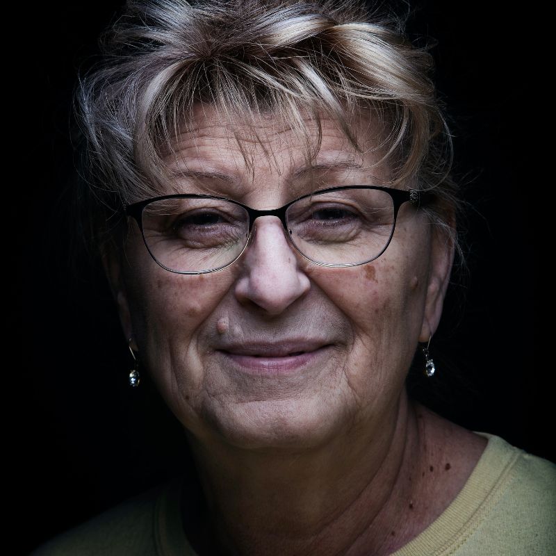 Older white woman with glasses, dangling diamond earrings, blonde hair, and a lime green t-shirt