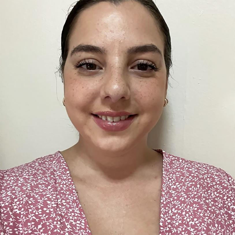 A woman who is smiling. She is wearing a pink and white v-neck shirt.