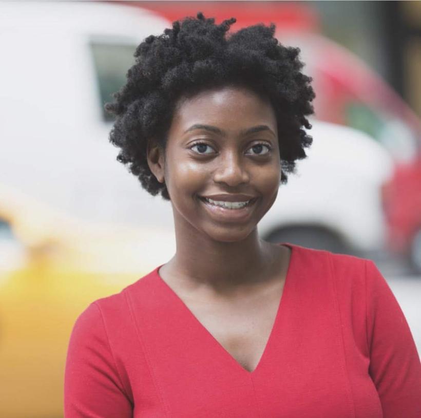 A black woman. She is smiling and wearing a red vneck sweater.