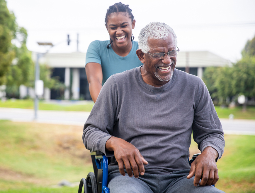 Black woman pushing Black man in wheelchair.