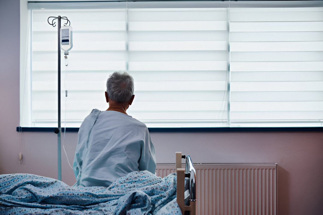 older man in hospital bed. he is looking out the window.