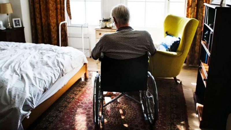 elderly man in wheelchair beside bed