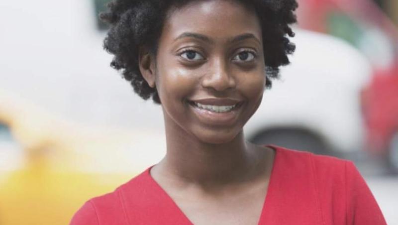 A black woman. She is smiling and wearing a red vneck sweater.