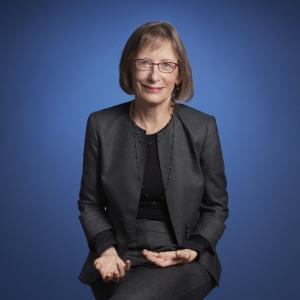 white woman with glasses and black suit sitting in chair 