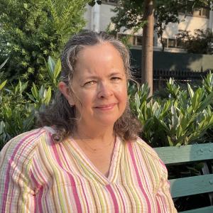 A woman sitting on a bench. She is wearing a striped shirt.