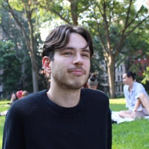A man with dark hair sitting in the park.