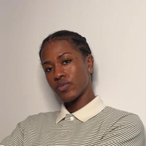 A black person with piercings and a striped polo shirt.