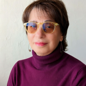A woman with shaded glasses, a short haircut, and a purple turtleneck.