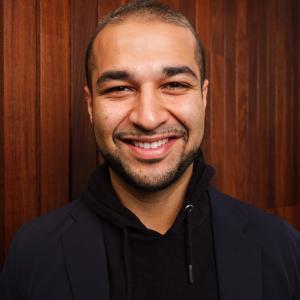 A man standing in front of a wooden back panel.